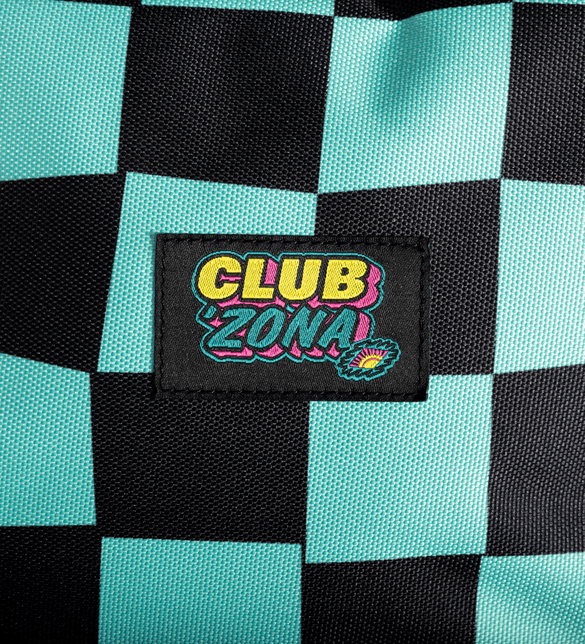 Close-up of a black and mint green checkered fabric Backpackwith a central embroidered patch reading 'CLUB ZONA' in yellow, pink, and blue.