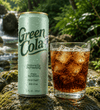 A Green Cola beverage can stands next to a clear glass filled with iced cola on a mossy rock, with a blurred outdoor waterfall and green foliage in the background.