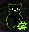 A black cat-shaped glow-in-the-dark product shown against a dark illustrated Halloween storefront background. The cat has a bright neon green glow around it.