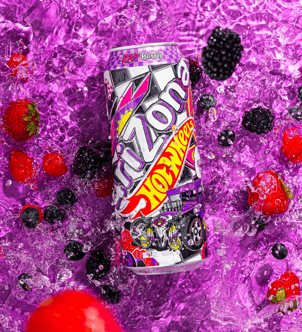 A can of Arizona Hot Wheels Energy Drink, flavor Ice Berry, is shown floating in clear liquid with ice cubes and fresh berries (strawberries, blackberries, blueberries) against a vibrant purple background.
