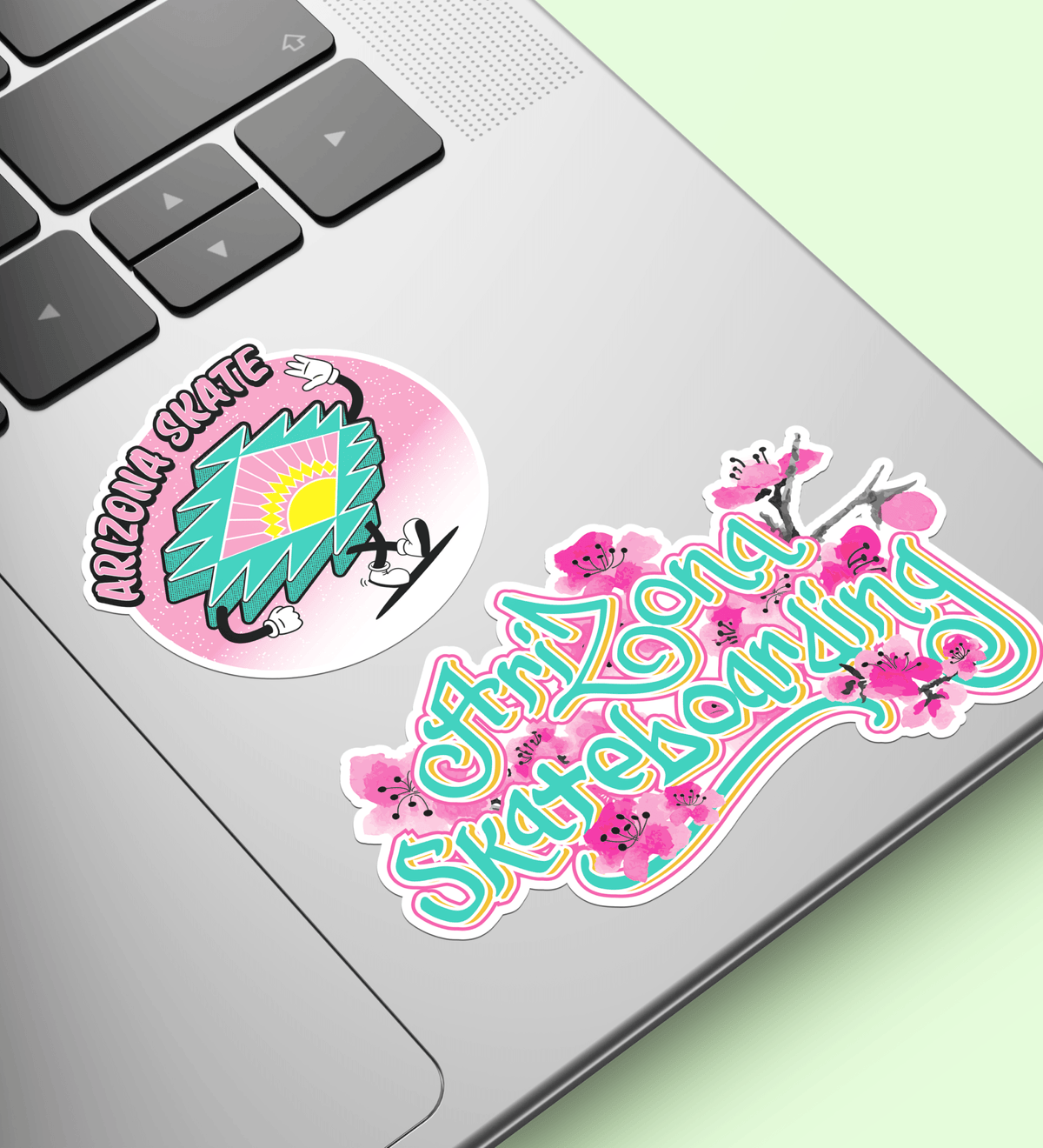 Two stickers on a laptop keyboard with 'Arizona Skate' and 'Arizona Skateboarding' designs.