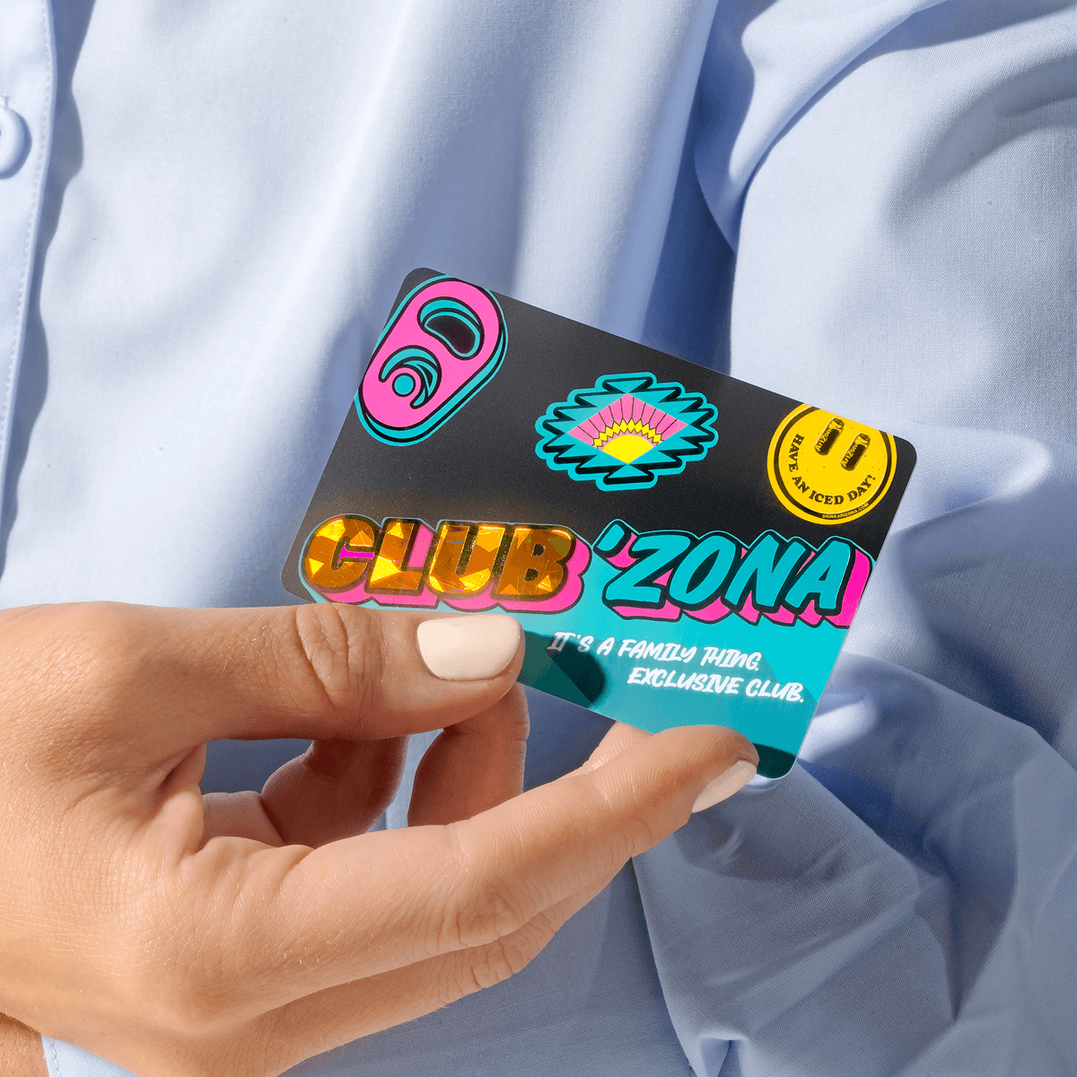 A hand holding a Club 'Zona membership card against a light blue button-down shirt background.