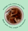 A top-down view of a glass filled with dark cola and ice cubes, centered on a light mint green background with decorative text reading 'Vintage cola scent and taste. Made with real, simple ingredients.