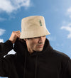 Man wearing a beige AZ bucket hat with a logo against a blue sky.