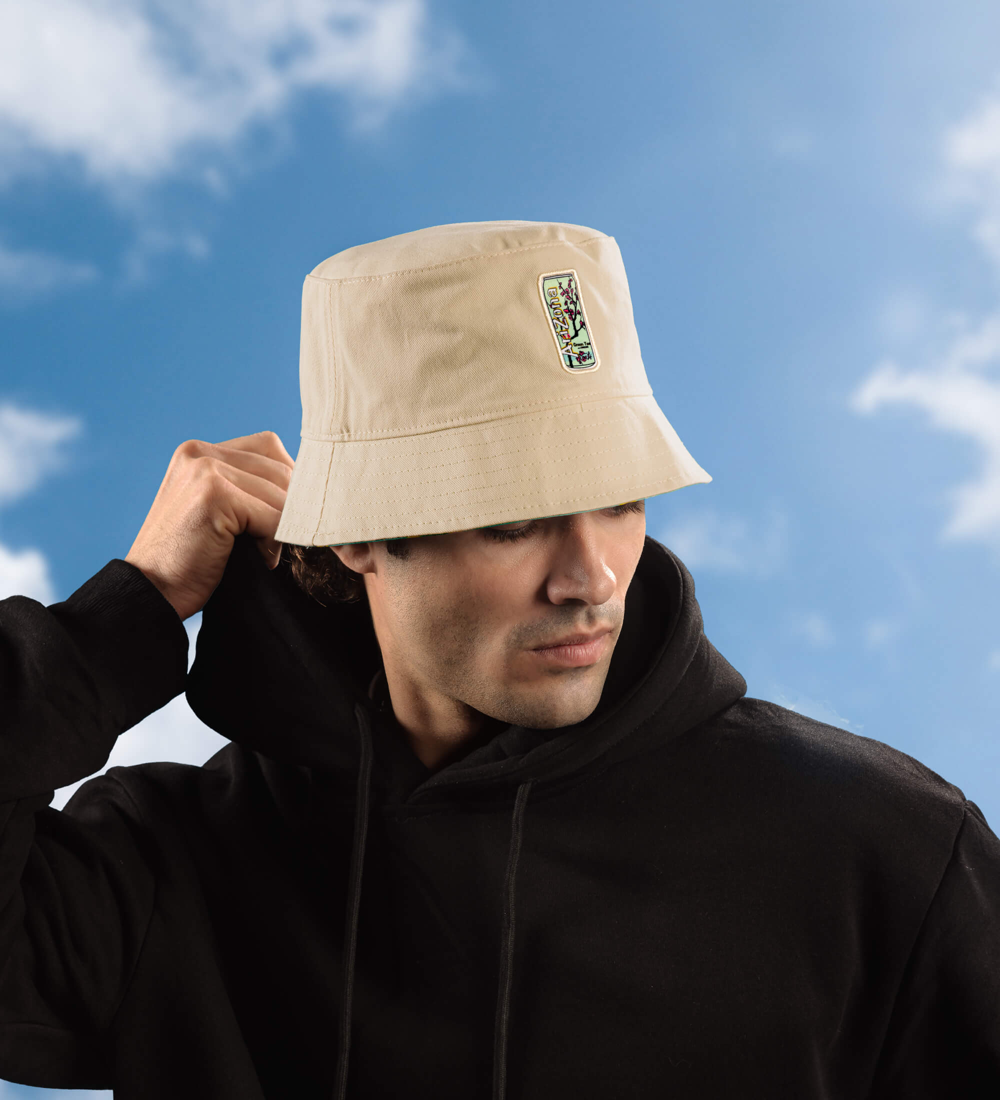 Man wearing a beige AZ bucket hat with a logo against a blue sky.