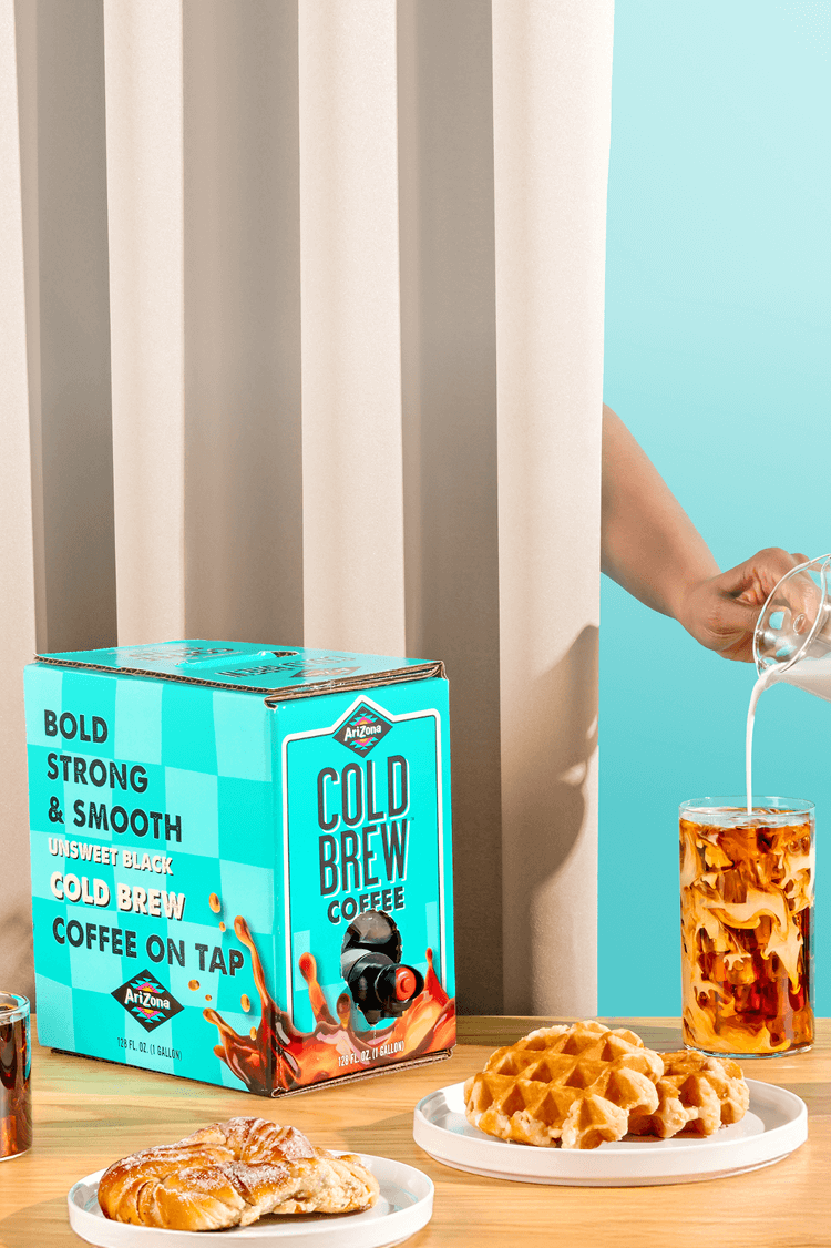 Cold brew coffee packaging with a glass of iced coffee and waffles on a table.