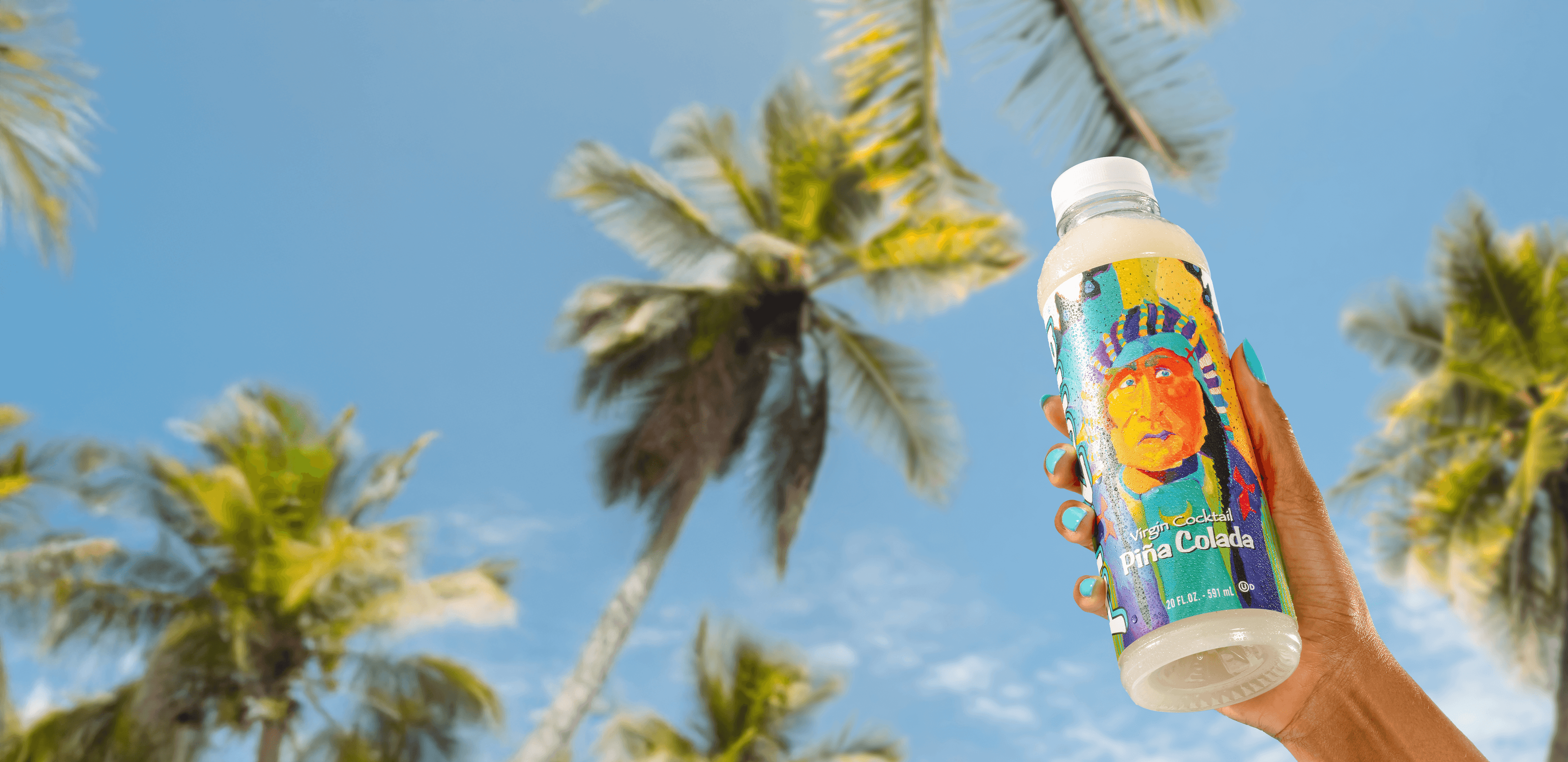 Hand holding a pina colada juice cocktail bottle against a palm tree and blue sky background