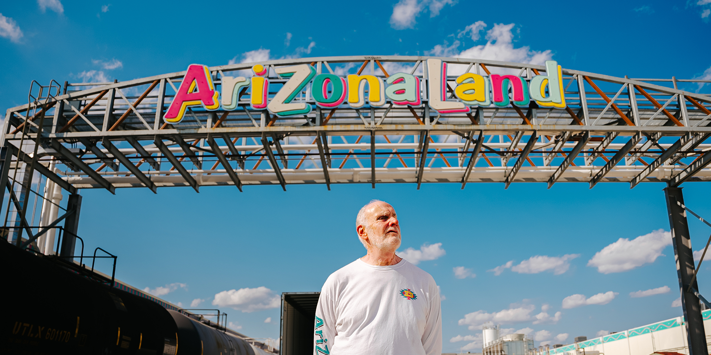 Don Vultaggio standing under a colorful 'Arizona Land' sign with a blue sky in the background