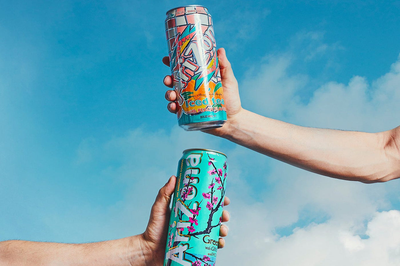 Two colorful AZ cans held up against a blue sky with clouds.