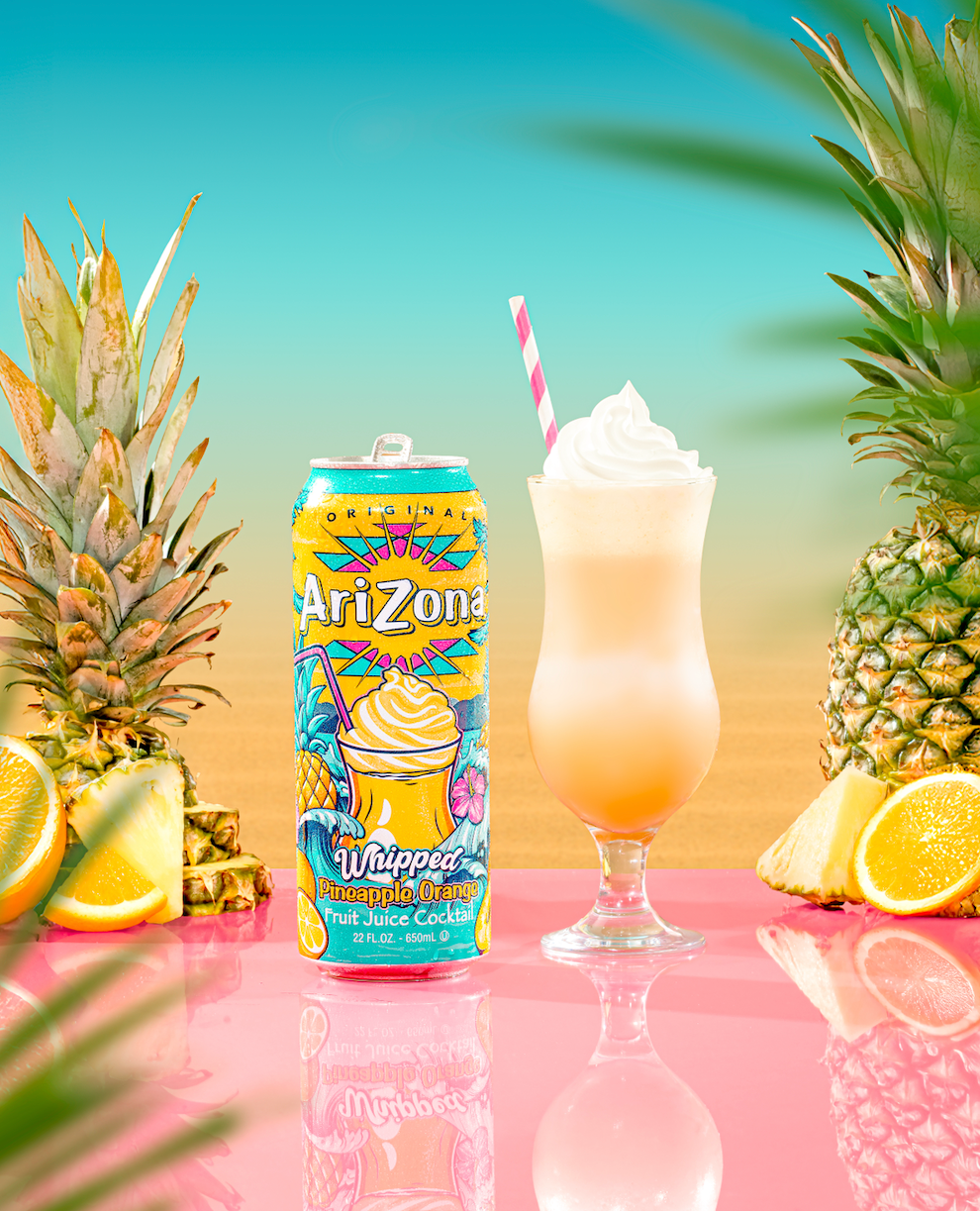 Arizona whipped pineapple drink can with a glass of the drink, pineapple, and lemon on a colorful background